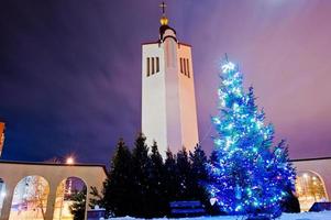 sino da igreja com árvore de ano novo com guirlanda brilhante à luz da lua na noite congelada foto