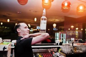 barman segura garrafa nos cotovelos da mão no bar foto