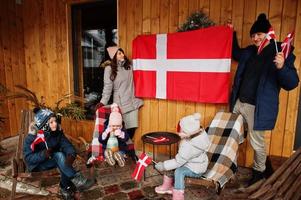 família com bandeiras da Dinamarca perto da casa de madeira. viajar para países escandinavos. o povo dinamarquês mais feliz. foto