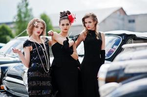 três jovem em estilo retrô vestido perto de carros antigos clássicos antigos. foto