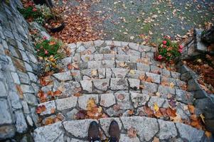 sapatos de homem ficam nas escadas de pedra com folhas de outono foto