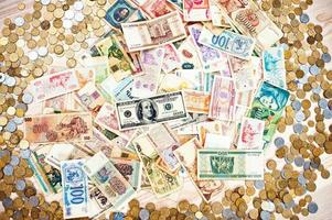 muitas moedas e dinheiro de diferentes países em fundo de madeira foto