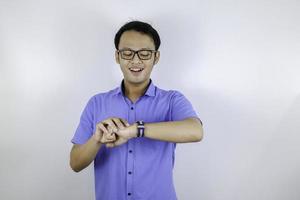 jovem asiático usa camisa azul está feliz e sorrindo ao apontar e olhar para o relógio isolado sobre fundo branco foto