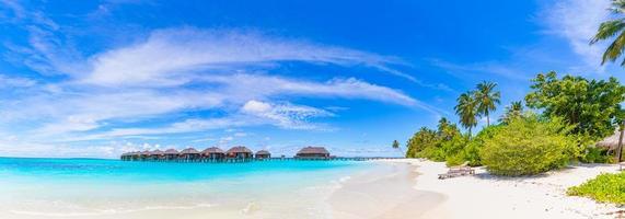 panorama incrível em maldivas. luxo resort vilas vista do mar com palmeiras, areia branca e céu azul. bela paisagem de verão. fundo de praia incrível para férias de férias. conceito de ilha paradisíaca foto