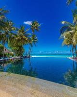 paisagem de turismo ao ar livre. luxuoso resort de praia com piscina e cadeiras de praia ou espreguiçadeiras sob guarda-sóis com palmeiras e céu azul. conceito de fundo de viagens e férias de verão foto