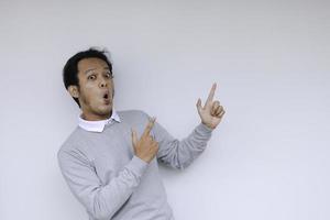 jovem asiático waer camisa branca está surpreso e gritando uau com apontando para a direita com o dedo isolado no fundo cinza com espaço de cópia para o seu texto. foto