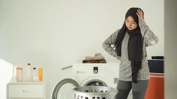 jovem mulher asiática chateada ao ver cesta de roupas sujas em casa foto