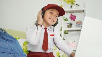 menina asiática do ensino fundamental estudando online em casa ouvindo usando fone de ouvido foto