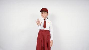 menina asiática da escola primária gesticulando parada isolada no fundo branco foto