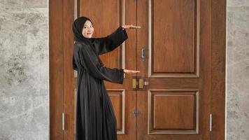mulher de vestido preto muçulmano, apontando inexpressivamente para o lado na frente da porta foto