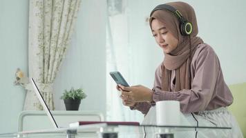 mulher asiática em hijab procurando inspiração no smartphone enquanto ouve em fones de ouvido foto