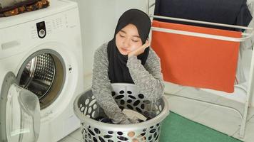 mulher asiática vestindo hijab cansado da pilha de roupas sujas em casa foto