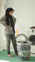 jovem mulher asiática olhando para a cesta de roupas sujas em casa foto