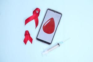 fita vermelha e sangue no símbolo da tela do smartphone contra hiv isolado em fundo azul foto