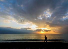 sochi, rússia. 28 de setembro de 2016. homem andando sozinho na praia do mar ao pôr do sol. foto