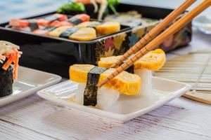 comendo sushi tamagoyaki ou ovo doce no envoltório de arroz e algas no prato quadrado branco com pauzinhos. deliciosa comida japonesa. foto