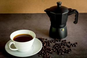 close-up quente de café preto e pote de moka e grãos de café na mesa escura. benefício do conceito de café. foto