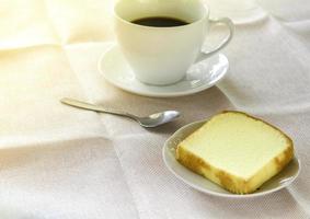 pedaço de bolo de manteiga no prato branco servido com uma xícara de café preto. vezes para relaxar o conceito. foto