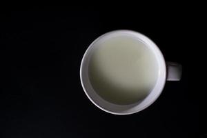 vista superior do copo branco de leite em fundo preto com espaço de cópia. alta proteína e cálcio. bebida saudável. foto