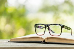livro e óculos na mesa de madeira com natureza verde abstrata desfocar o fundo. conceito de leitura e educação
