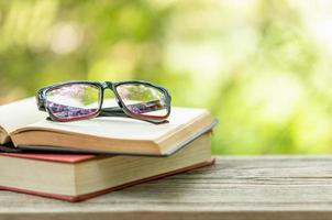 livro e óculos na mesa de madeira com natureza verde abstrata desfocar o fundo. conceito de leitura e educação foto