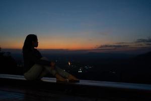 silhueta de mulher sentada no terraço e olhando o pôr do sol sobre a montanha foto