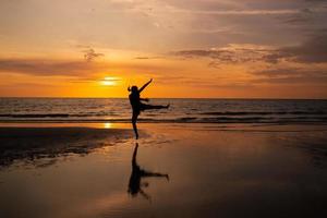 silhueta de mulher pulando na praia ao pôr do sol foto