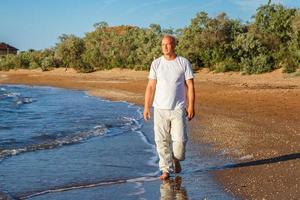 homem careca feliz andando na praia em roupas brancas foto