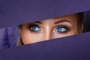 os olhos das mulheres bonitas olham no buraco do papel, maquiagem brilhante, foto