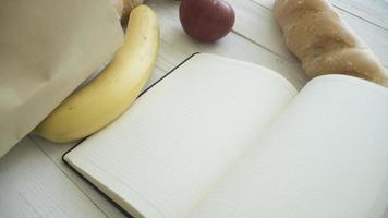 saco de papel cheio de produtos alimentares com caderninho em branco na mesa de madeira, vista superior foto