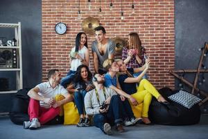 retrato de grupo de meninos e meninas multiétnicas com roupas coloridas da moda segurando amigo posando em uma parede de tijolos, pessoas de estilo urbano se divertindo, conceitos sobre estilo de vida de união juvenil foto