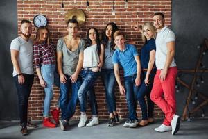 retrato de grupo de meninos e meninas multiétnicas com roupas coloridas da moda segurando amigo posando em uma parede de tijolos, pessoas de estilo urbano se divertindo, conceitos sobre estilo de vida de união juvenil foto