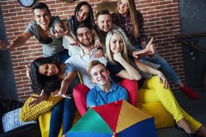 retrato de grupo de meninos e meninas multiétnicas com roupas coloridas da moda segurando amigo posando em uma parede de tijolos, pessoas de estilo urbano se divertindo, conceitos sobre estilo de vida de união juvenil foto