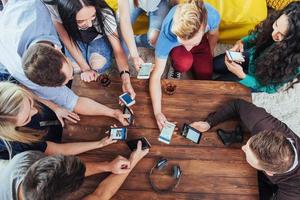 vista superior círculo de mãos usando telefone no café - cena interior viciada em celular de amigos multirraciais de cima - pessoas conectadas wifi na reunião de mesa de bar - conceito de trabalho em equipe foto