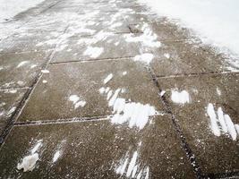 vento fez manchas de neve na superfície do pavimento escuro de azulejos foto