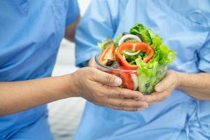 paciente asiático sênior ou idosa idosa comendo alimentos saudáveis de vegetais de café da manhã com esperança e feliz enquanto está sentado e com fome na cama no hospital. foto