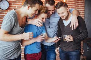 alegres velhos amigos se comunicam e observam o telefone, copos de uísque no pub. estilo de vida de entretenimento de conceito. pessoas conectadas por wifi em reunião de mesa de bar foto