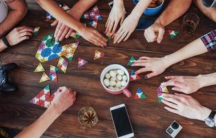 foto criativa de vista superior de amigos sentados à mesa de madeira. se divertindo jogando jogo de tabuleiro