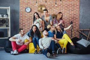 retrato de grupo de meninos e meninas multiétnicas com roupas coloridas da moda segurando amigo posando em uma parede de tijolos, pessoas de estilo urbano se divertindo, conceitos sobre estilo de vida de união juvenil foto