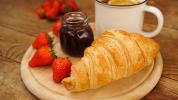 lanches de pausa para o chá. chá de limão, croissant, pote de geléia e morangos frescos. foto