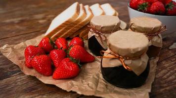 fatias de pão e delicioso pote de geléia de morango e frutas frescas na madeira foto