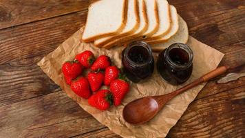 fatias de pão e delicioso pote de geléia de morango e frutas frescas na madeira foto