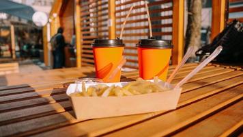 comida rápida. dois copos de papel laranja e batatas fritas com molho na mesa de madeira foto