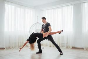 jovem casal dançando música latina. bachata, merengue, salsa. duas pose de elegância no quarto branco foto