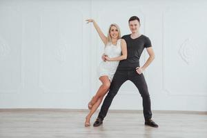 jovem casal dançando música latina. bachata, merengue, salsa. duas pose de elegância no quarto branco foto