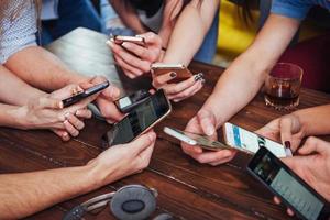 vista superior círculo de mãos usando telefone no café - cena interior viciada em celular de amigos multirraciais de cima - pessoas conectadas wifi na reunião de mesa de bar - conceito de trabalho em equipe foto