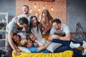 retrato de grupo de meninos e meninas multiétnicas com roupas coloridas da moda segurando amigo posando em uma parede de tijolos, pessoas de estilo urbano se divertindo, conceitos sobre estilo de vida de união juvenil foto