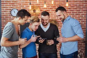 alegres velhos amigos se comunicam e observam o telefone, copos de uísque no pub. estilo de vida de entretenimento de conceito. pessoas conectadas por wifi em reunião de mesa de bar foto