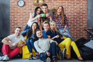 retrato de grupo de meninos e meninas multiétnicas com roupas coloridas da moda segurando amigo posando em uma parede de tijolos, pessoas de estilo urbano se divertindo, conceitos sobre estilo de vida de união juvenil foto