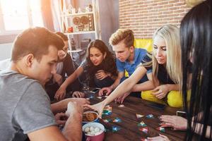 grupo de amigos criativos sentados à mesa de madeira. pessoas se divertindo jogando jogo de tabuleiro foto